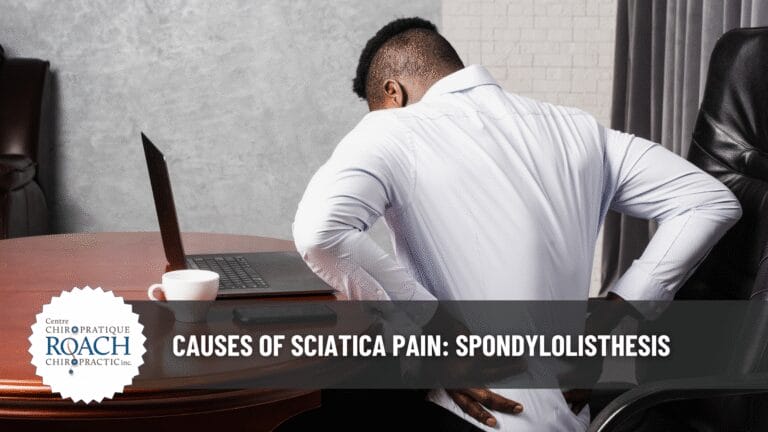 a man sitting at a table holding his lower back, experiencing spondylolisthesis