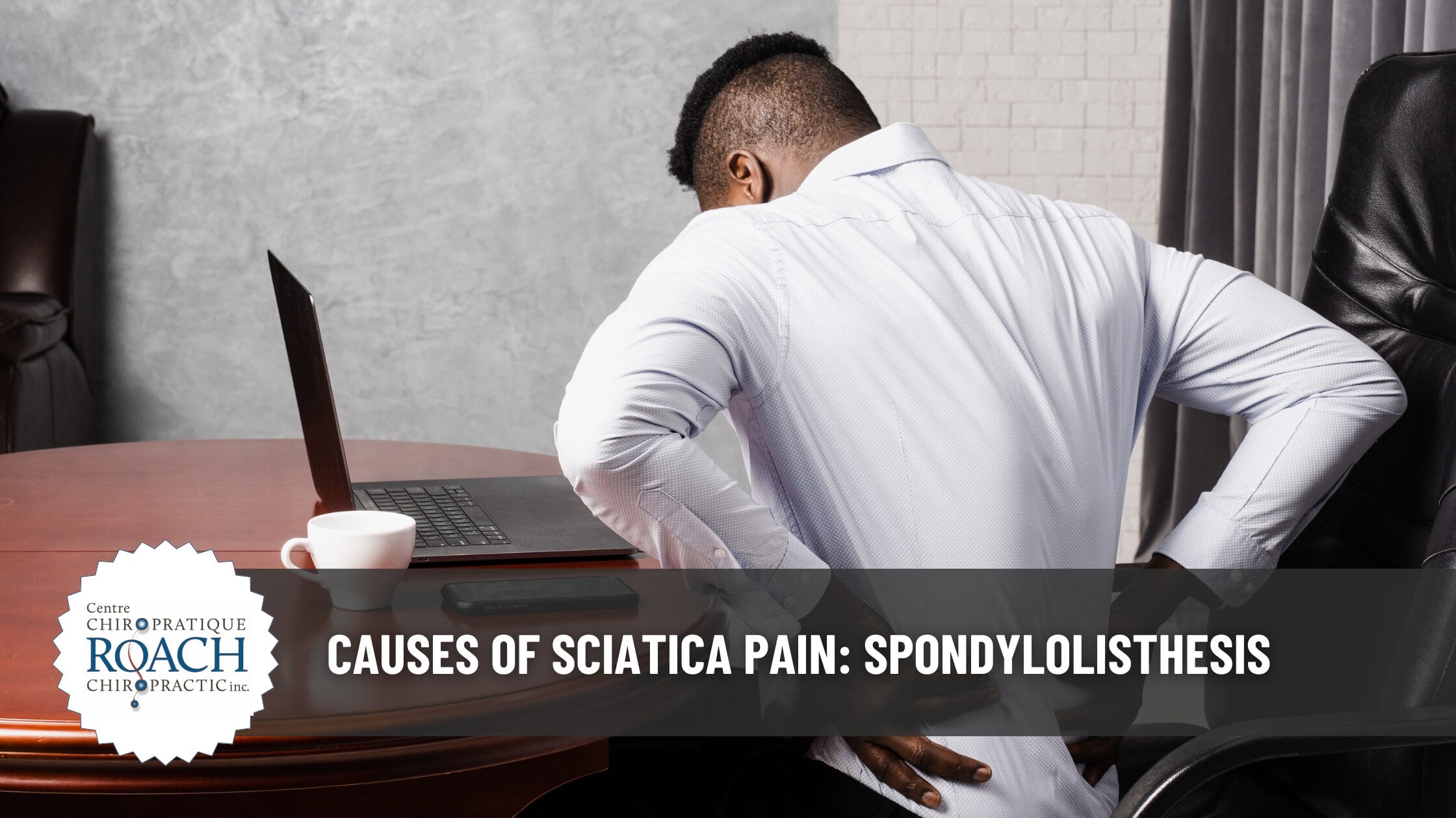 a man sitting at a table holding his lower back, experiencing spondylolisthesis